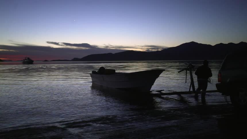 Man pushes boat into sea at sunset