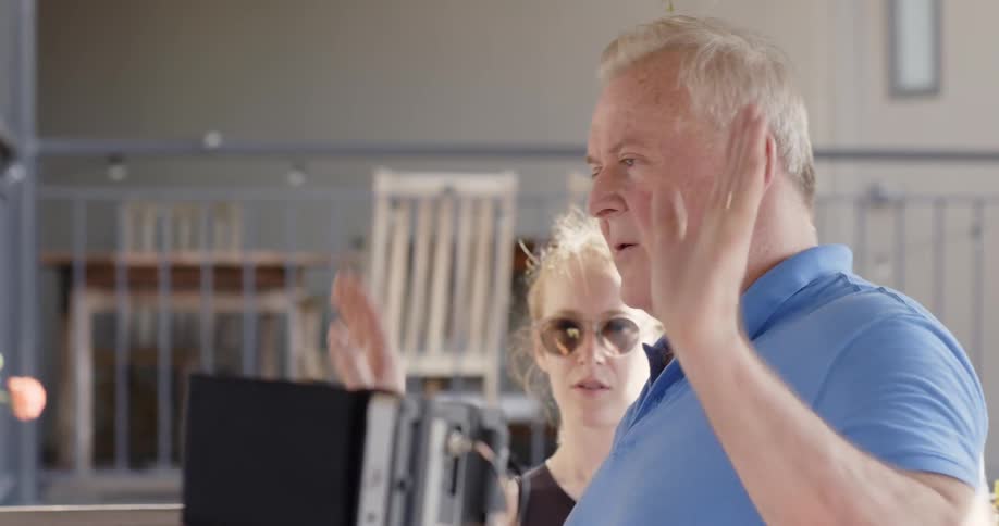 An older man talks and gestures next to a young woman