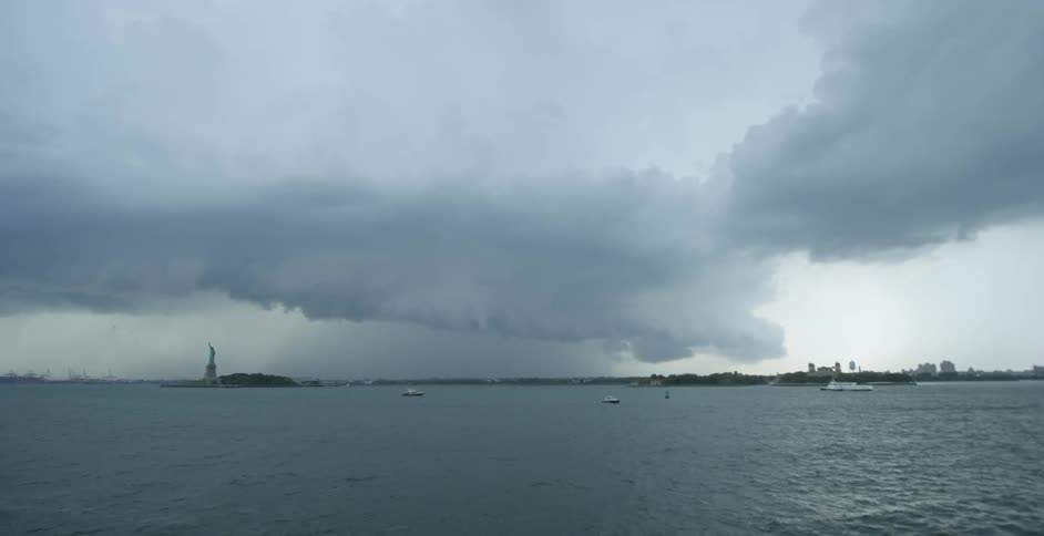 Boats float near the statue of liberty on a cloudy day