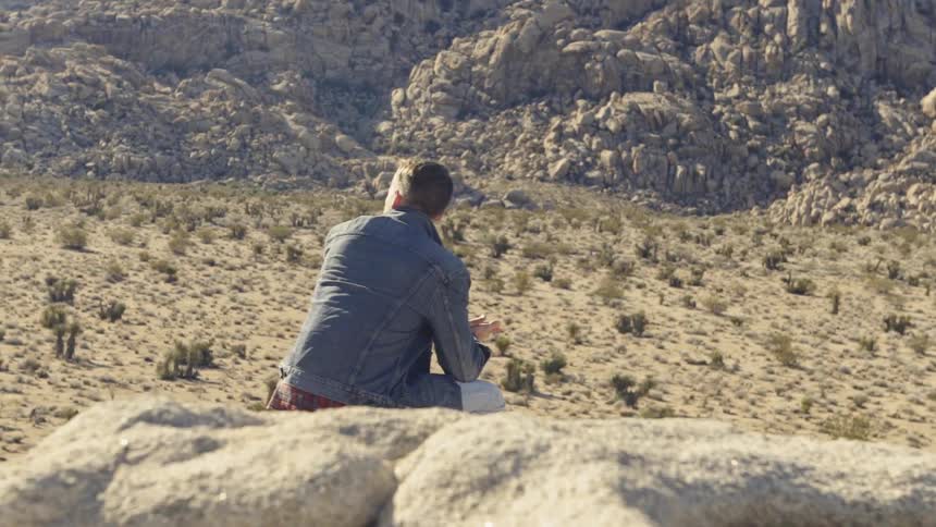 A hiker sits on a rock in a desert