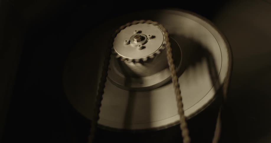A chain spins a gear attached to another chain in a dark room
