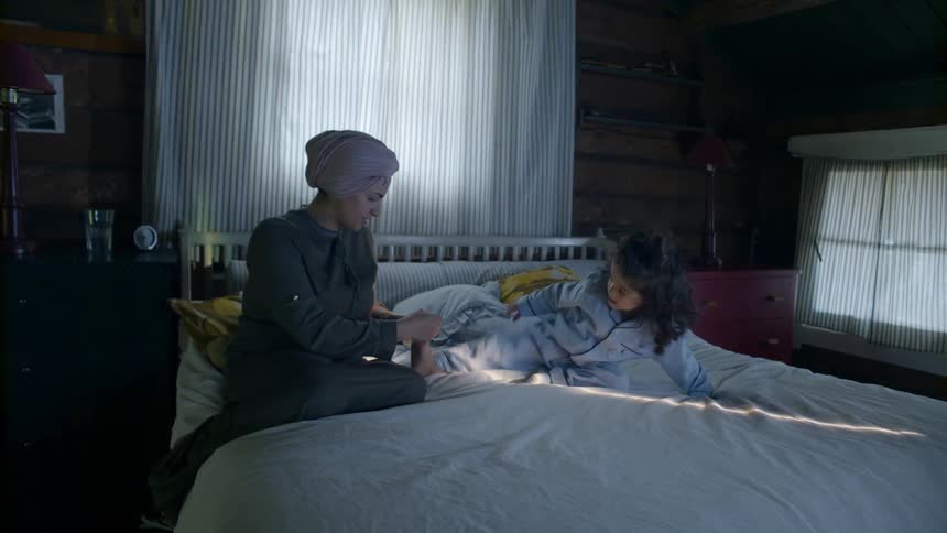 Woman sits on the edge of a bed as a young child climbs around on it