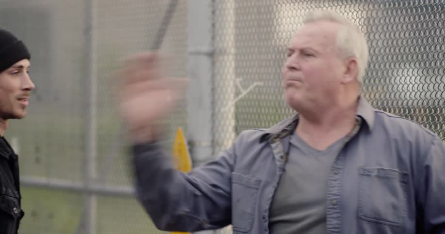 Two men planning fight choreography near a fence