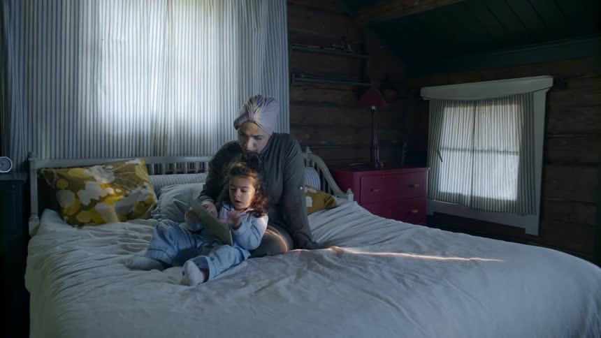 A child and woman look at a book together in bed