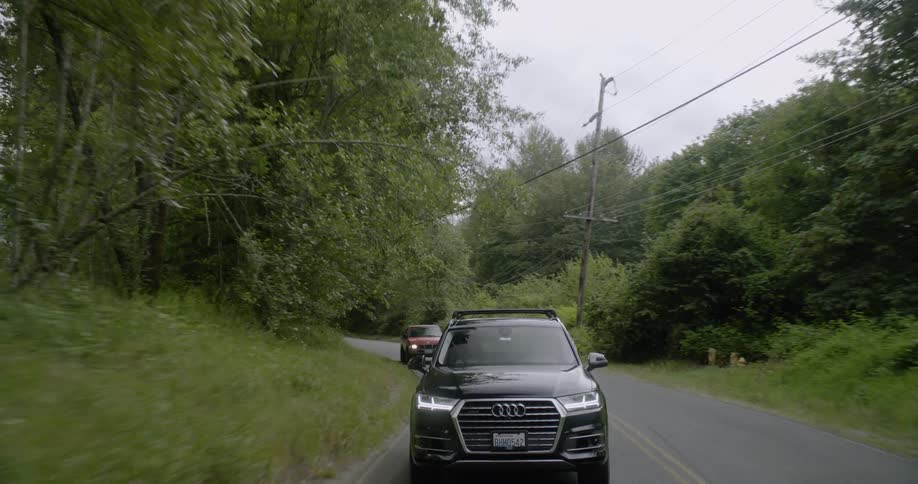 Two cars travel down the road near the trees