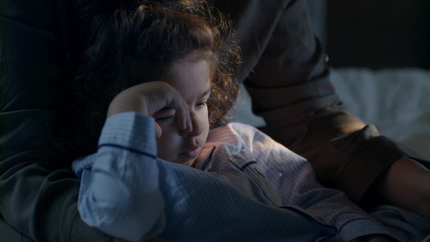 A child is falling asleep in bed with a parent
