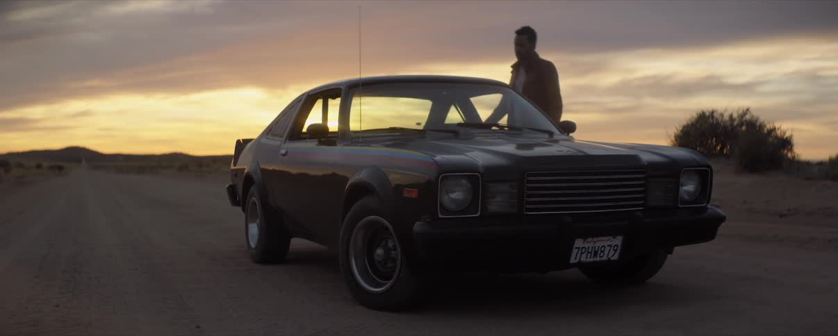 Man walks to a black car in the desert at sunset and gets in