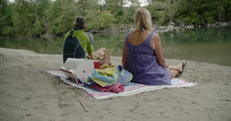 Man and woman blow bubbles sitting next to a stream