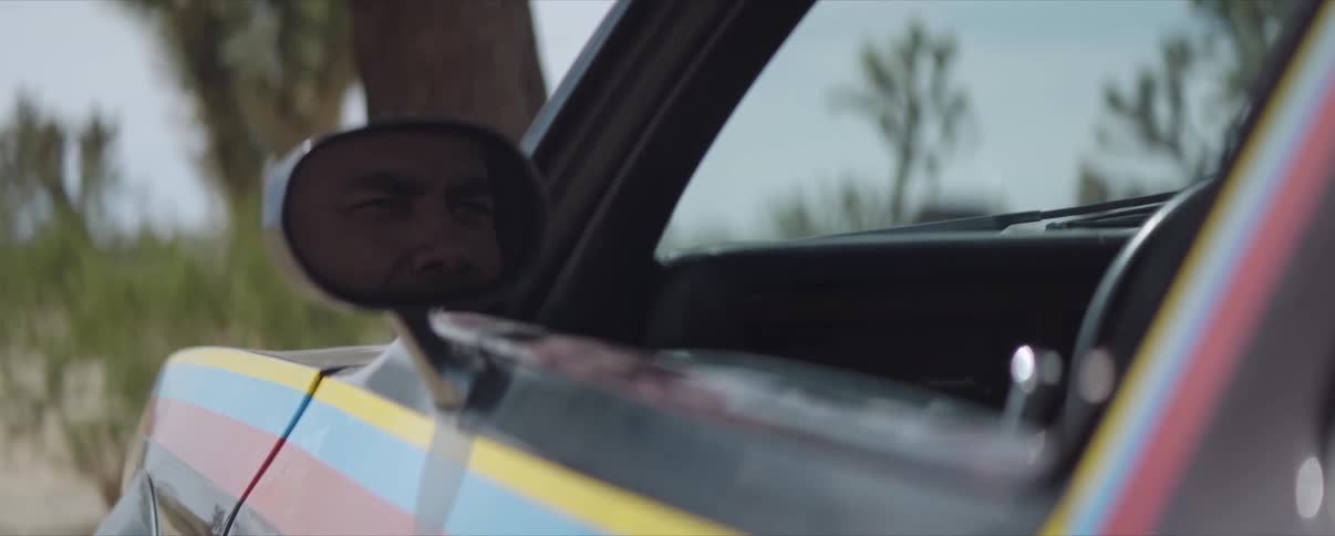 A man's face is reflected in the sideview mirror of a car