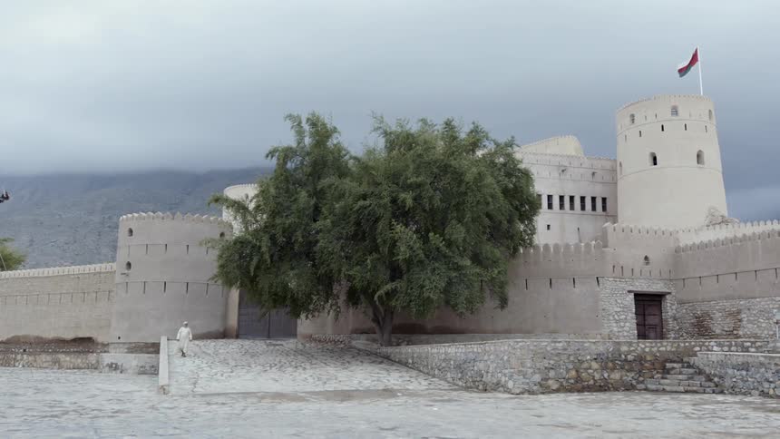 Man in robes walks near old-looking building with pillars