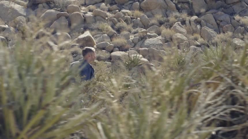 A man is running in the desert near a pile of rocks