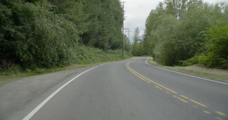 A car travels on a rural tree lined road