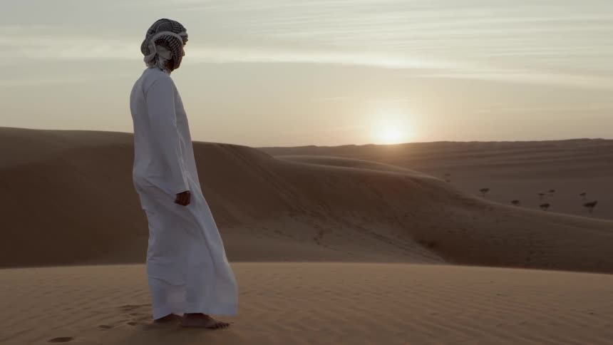 Man in a white gown stands in the desert