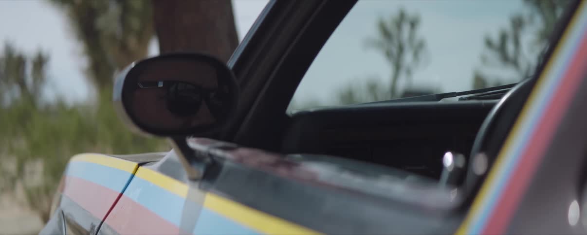 A man closes a car door and puts on sunglasses