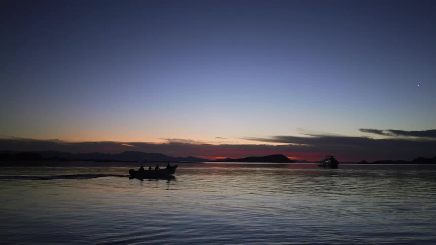 A small boat filled with people is traveling on a river at dusk