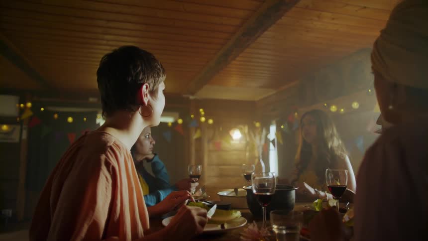 Woman sitting on table eats and look at her friend in a room