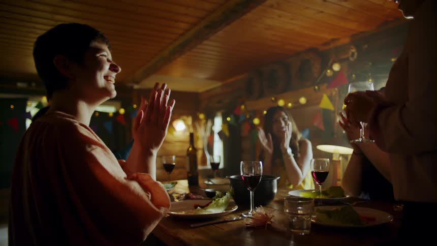 Women sit around the table and clap then they toast their wine glasses