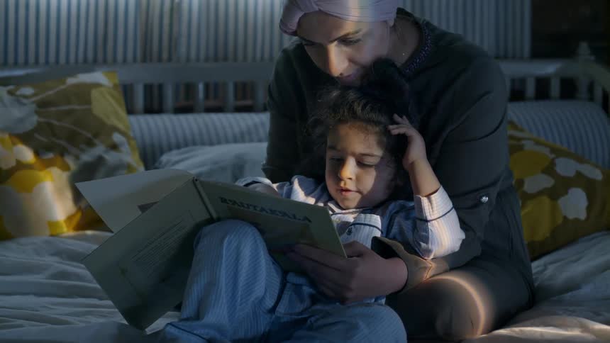Woman and child sit on a bed as they read a book