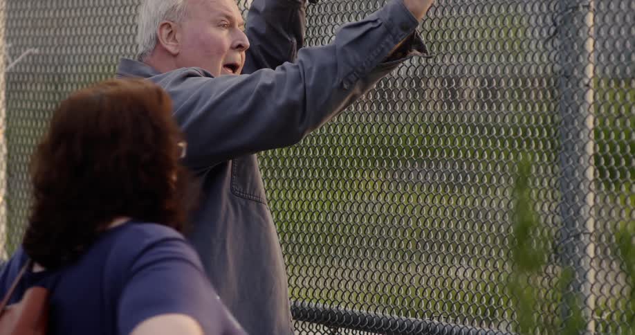 A woman walks up to and then away from a man leaning on a fence