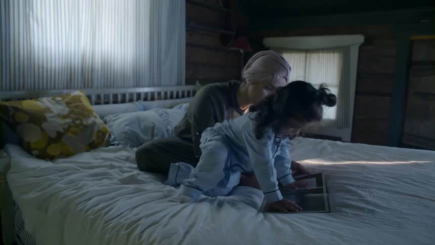 A woman and girl sit on the bed reading a book