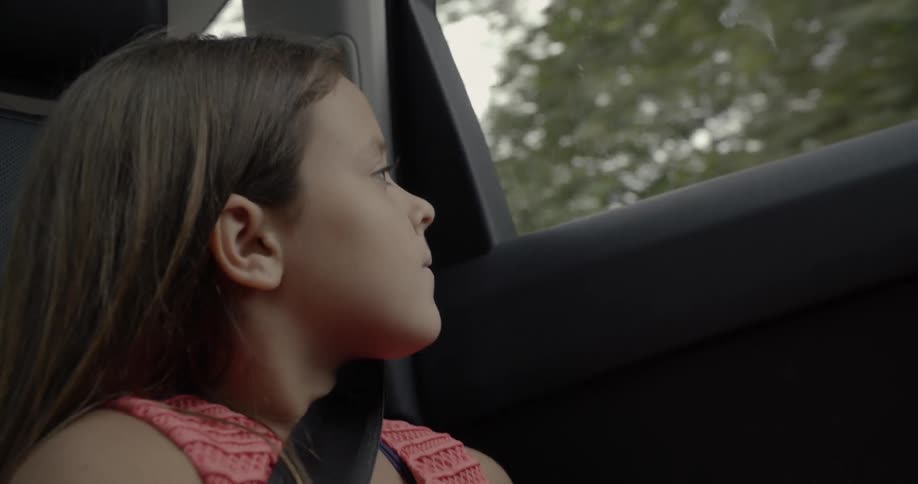 A young girl looks out the window of a moving car