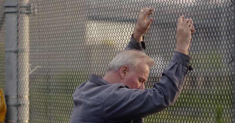 Man stands while holding onto chain link fence