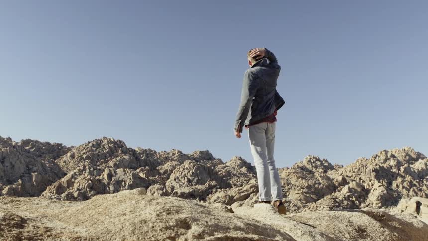 A young man looks out to the arid hillside under clean blue skies