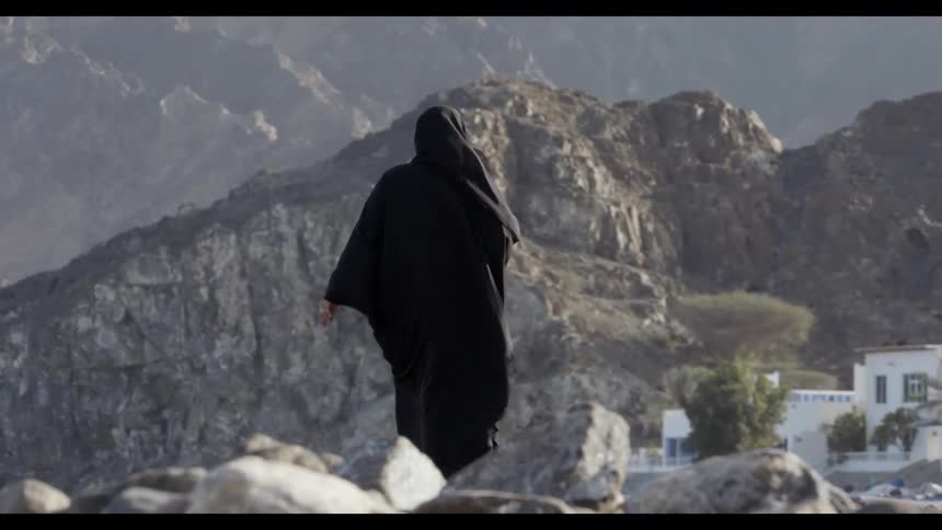 Man in black robes walks on rocky mountain