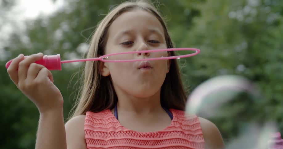 A child is blowing bubbles near the trees
