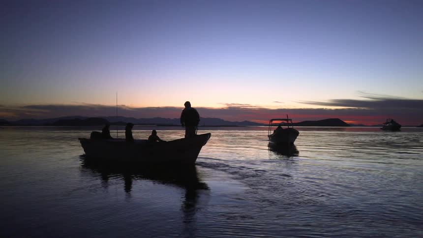 Silhouetted boats float on a rippling lake at dusk