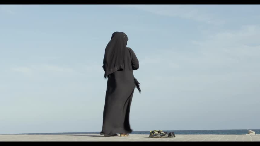 A person wearing black robes and a head covering stands in the wind