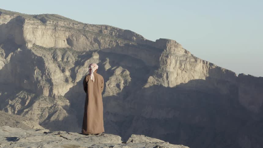 A person in a religious garb looks over a mountain scene