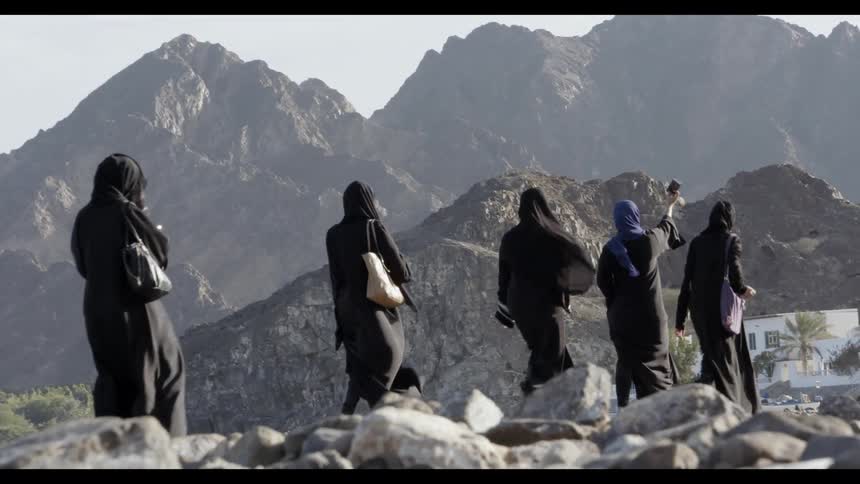 Women in traditional long tunics walk through a rocky scenery