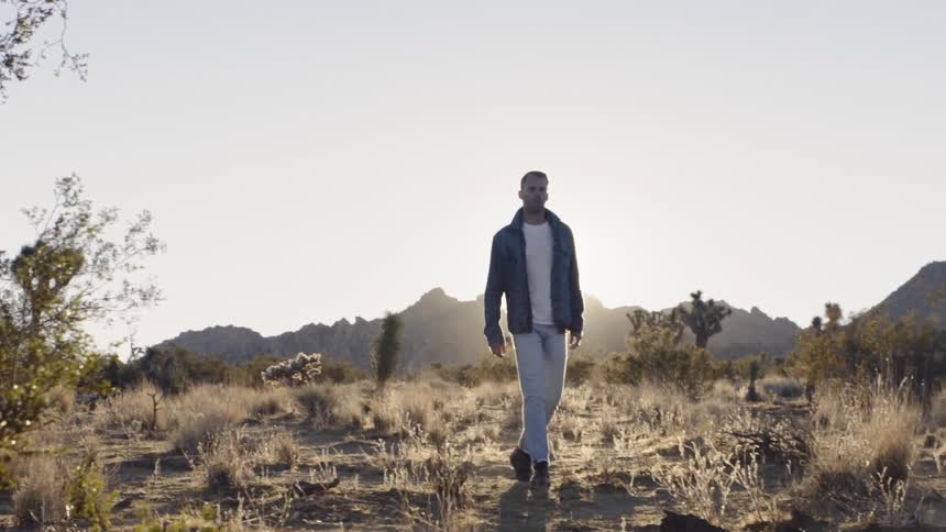 A man in a denim jacket walks on an arid landscape