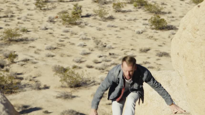 A man is climbing up the rocks near the desert