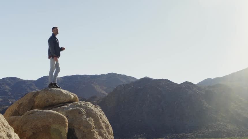 A hiker stands on a boulder in mountains