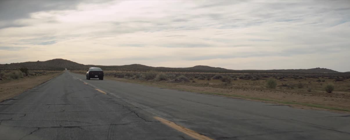 Car drives down on desert road on a cloudy day