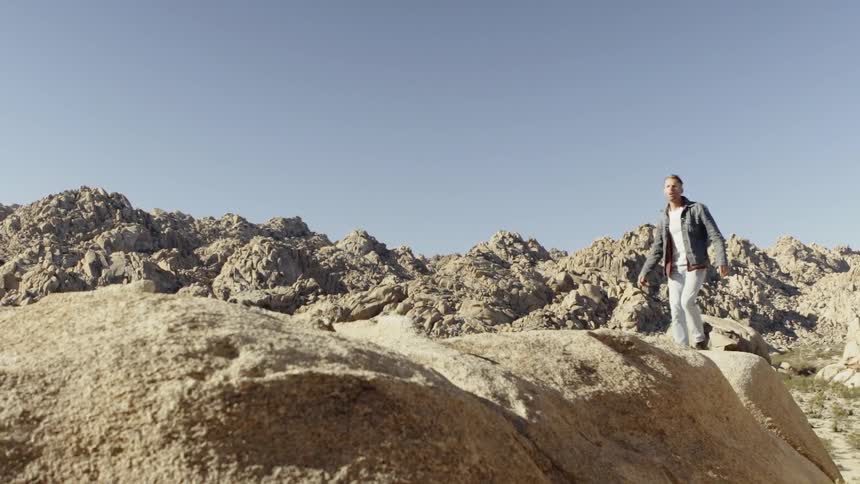 A man in a denim jacket scrambles up an arid set of rocks