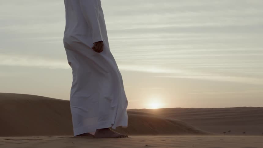A man in traditional garments stands peacefully in the desert