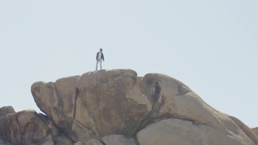A man is standing on a large rock outdoors