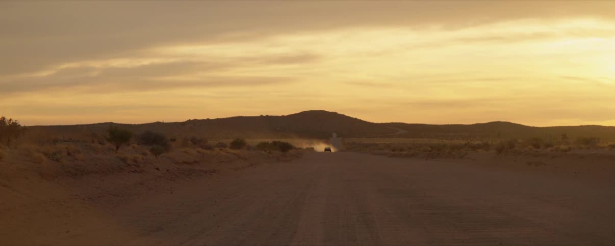 Car drives through desert at sunset