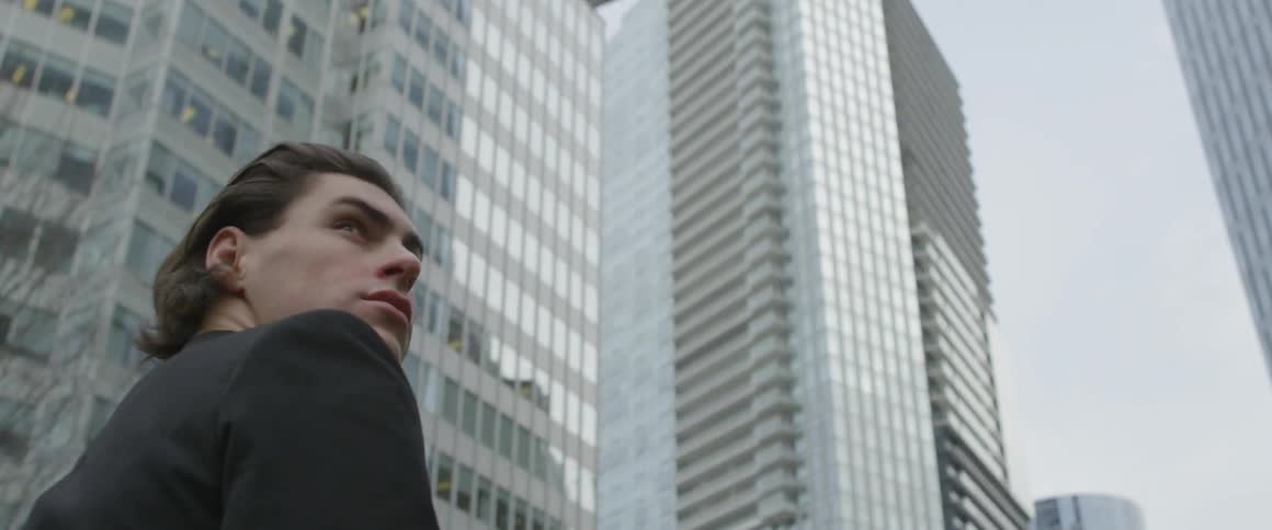 Young man walking down city street turning and looking up at a building behind him