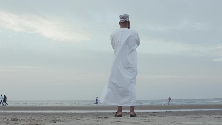 A man in flowing white robes stands on the beach