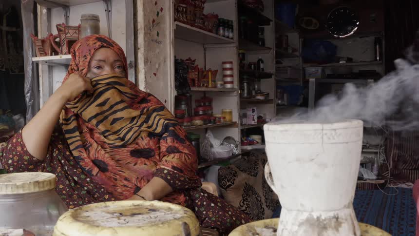 Woman in headscarf sits and covers her face while boiling pot
