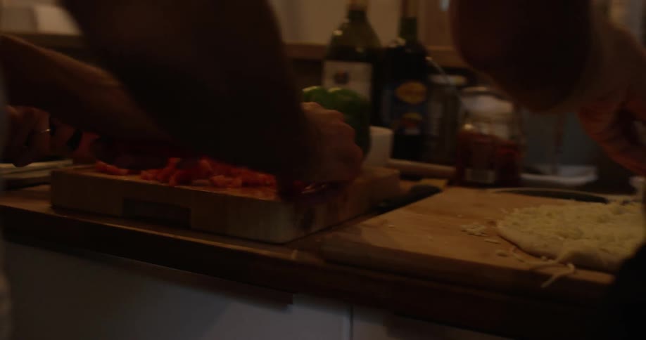 People standing side by side at a kitchen counter making a pizza