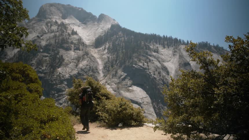Hiker carrying backpack walks dirt path on way to mountain