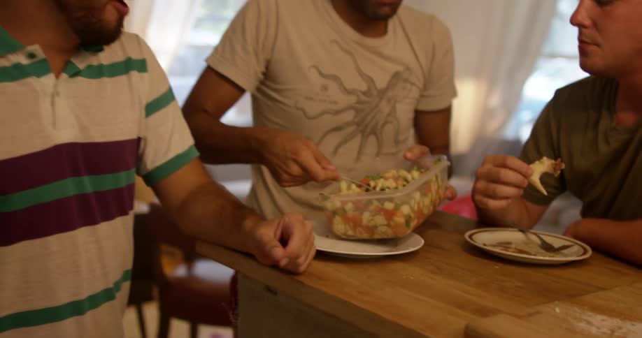 A group of people sitting around a kitchen island talking, eating and passing food