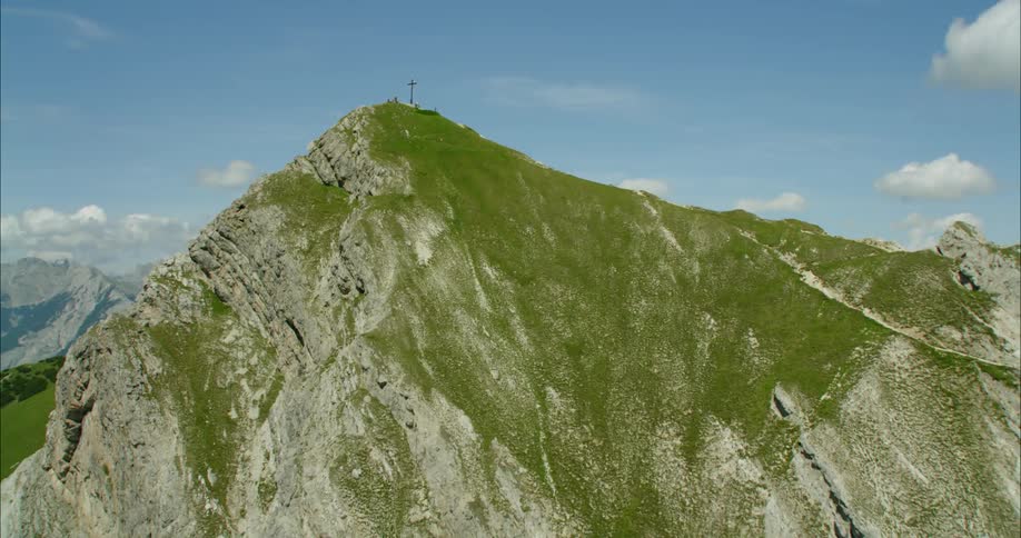 The tall green mountain has a cross at the top