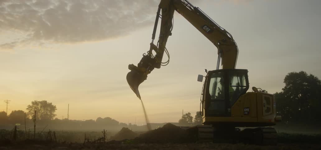 Crane drops dirt in field at sunset