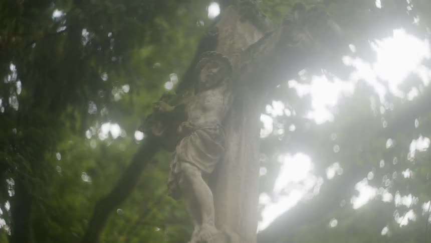 Statue of jesus on the cross with light shining through tree canopy